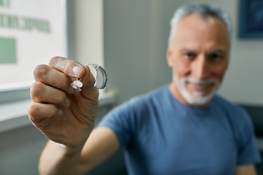Man holding up a modern behind-the-ear hearing aid to show its compact, advanced design