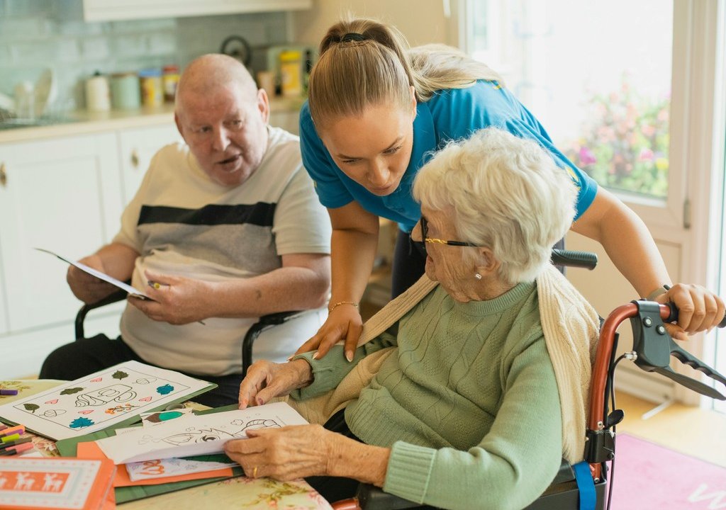 Caregiver assisting an elderly couple with a coloring activity