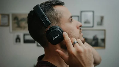 Man wearing over-ear headphones with his hand cupped to his ear, listening closely, representing focused listening during a hearing evaluation