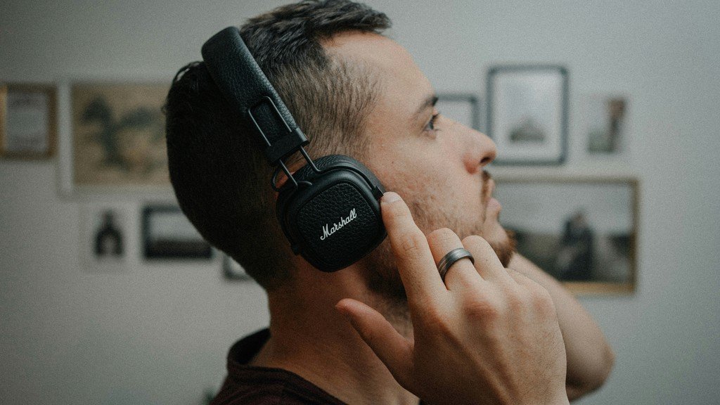 Man wearing over-ear headphones with his hand cupped to his ear, listening closely, representing focused listening during a hearing evaluation