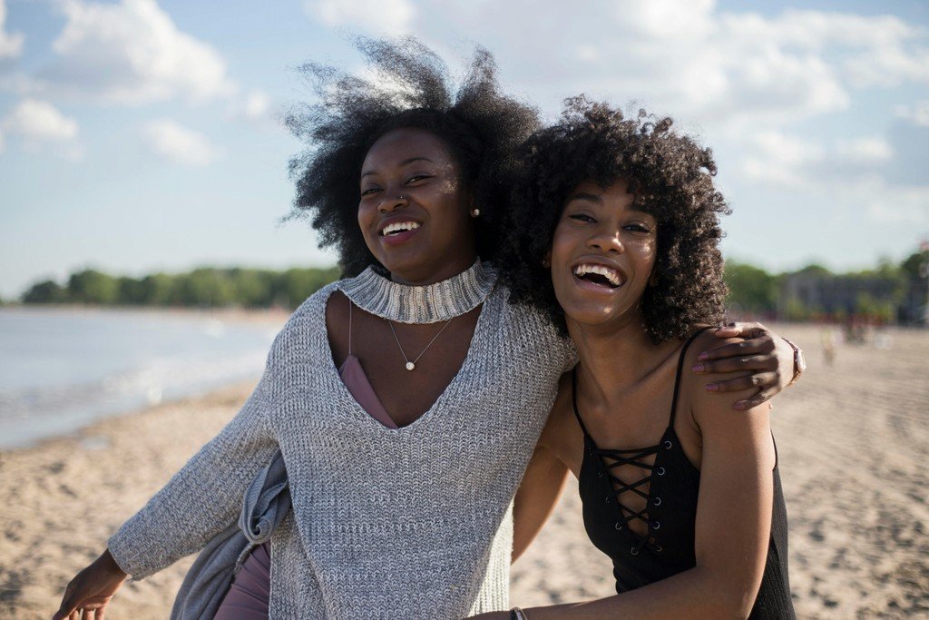 Two friends laughing together on a sunny beach, the kind of clear conversation restored by well-performing hearing aids