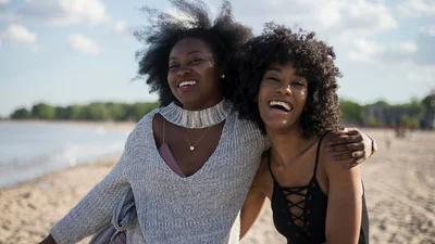 Two friends laughing together on a sunny beach, the kind of clear conversation restored by well-performing hearing aids