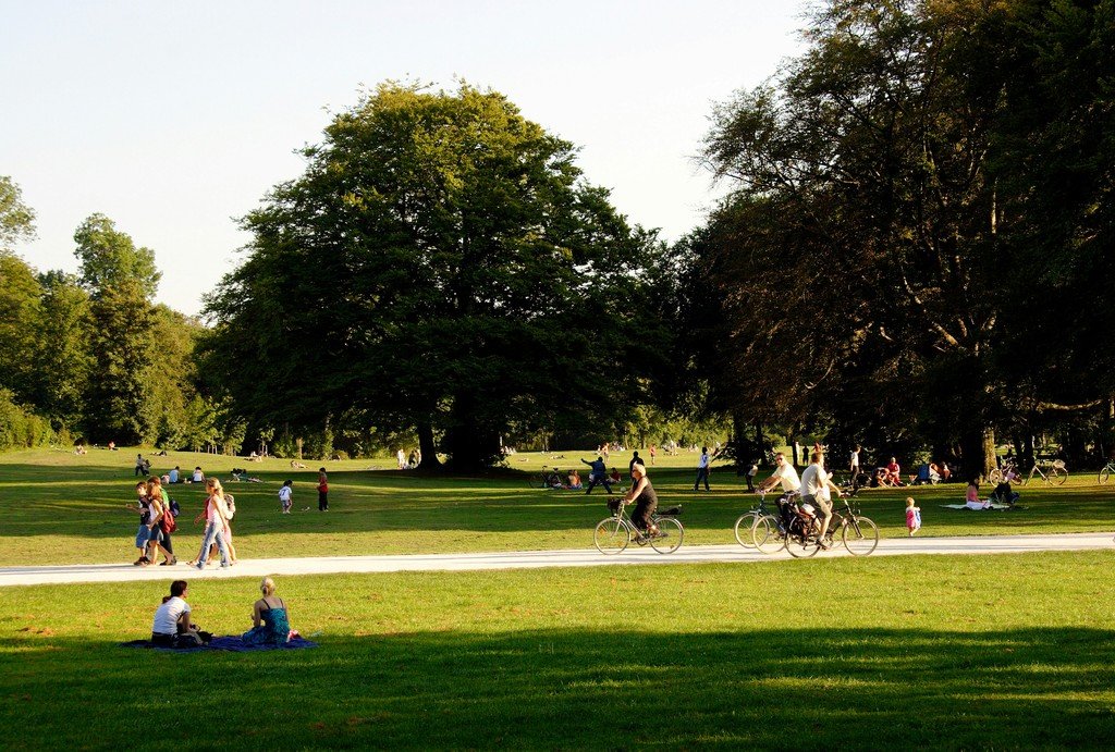 Families and friends relaxing, walking, and biking in a sunlit park, the kind of community gathering better hearing helps you enjoy fully