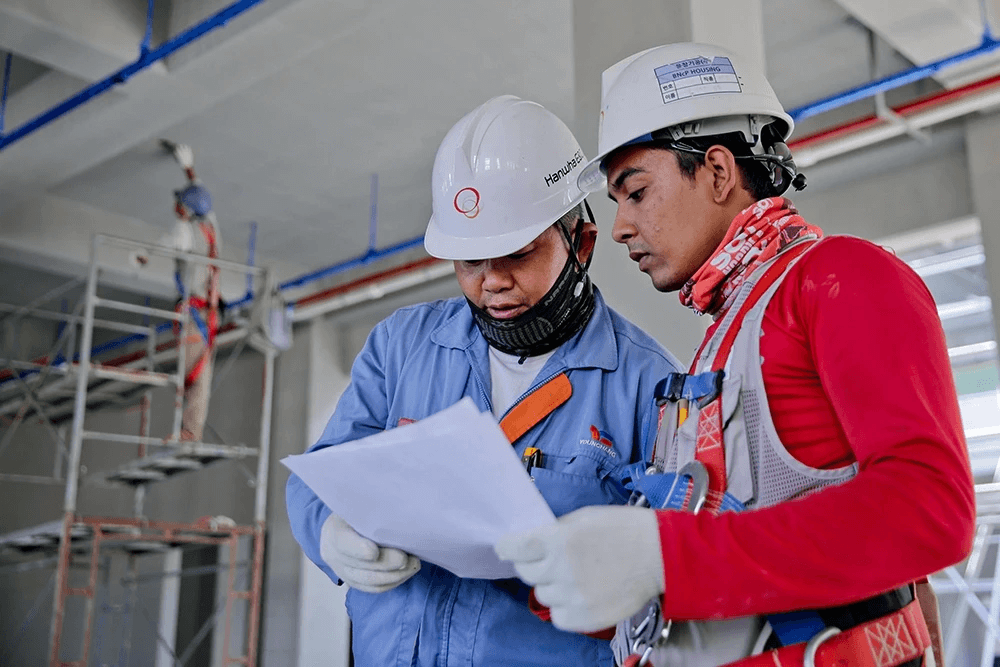 Construction workers in hard hats reviewing safety paperwork on a job site