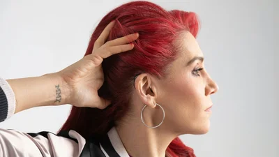 Close-up profile of a woman with red hair pulling her hair back to reveal a behind-the-ear hearing aid