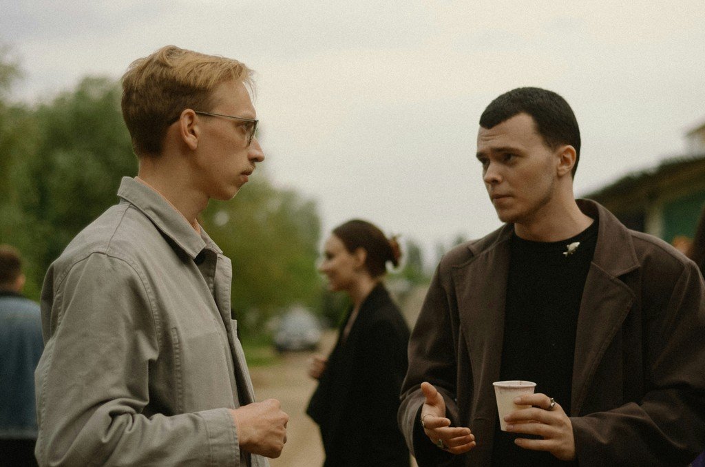 Two men having a conversation outdoors, one holding a drink