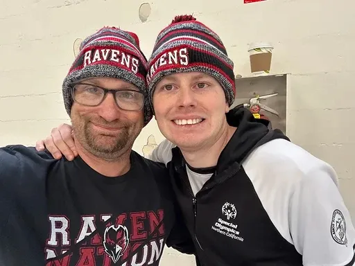 Two smiling patients wearing matching winter beanies with their arms around each other